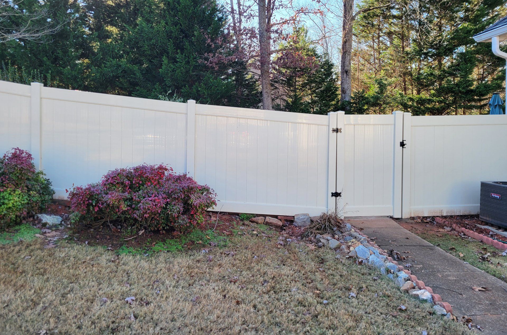 A white vinyl fence with a gate in the backyard of a house.