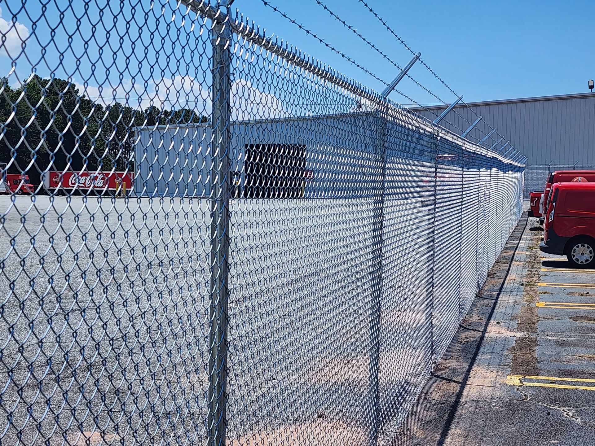A chain link fence with barbed wire surrounding a parking lot.