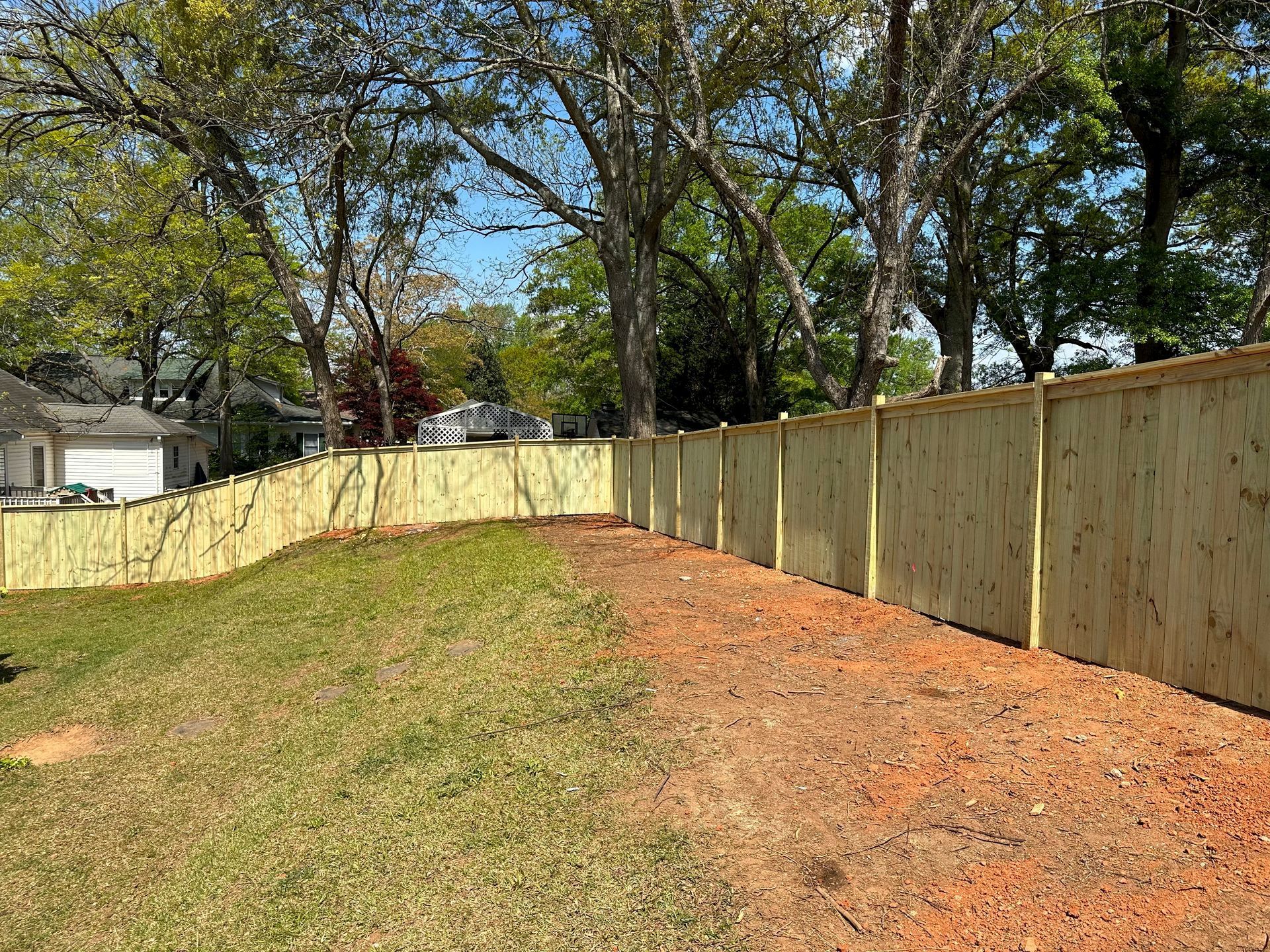 A wooden fence surrounds a grassy yard with trees in the background.