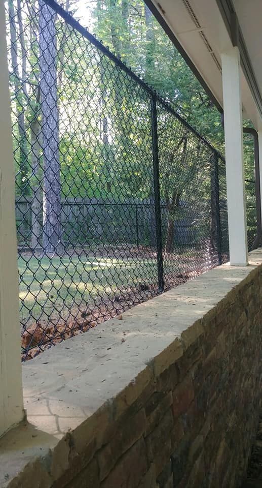 A chain link fence is surrounded by trees and a stone wall.