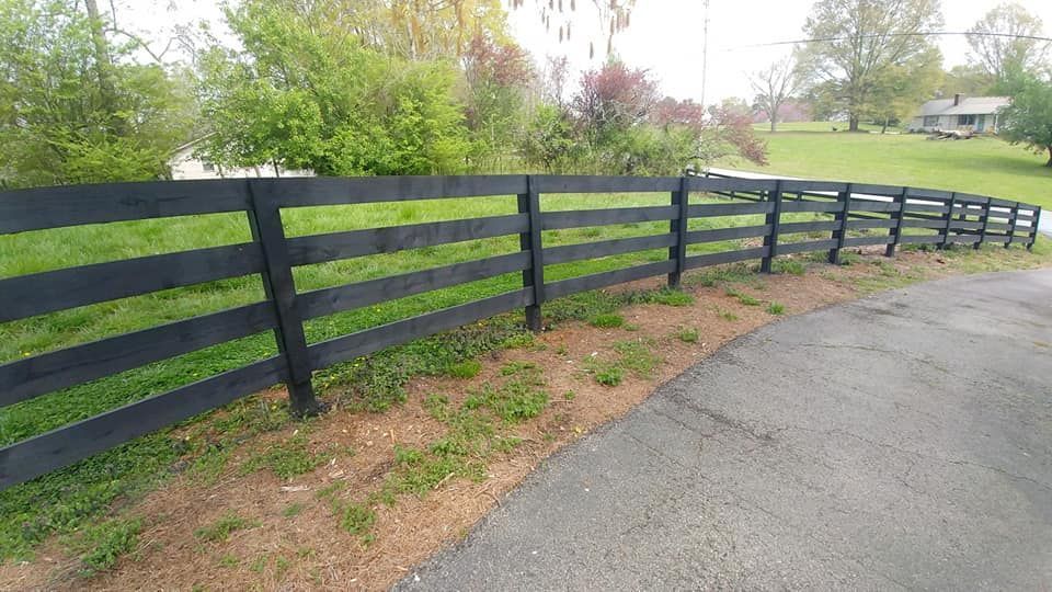 A black fence surrounds a grassy field next to a road.