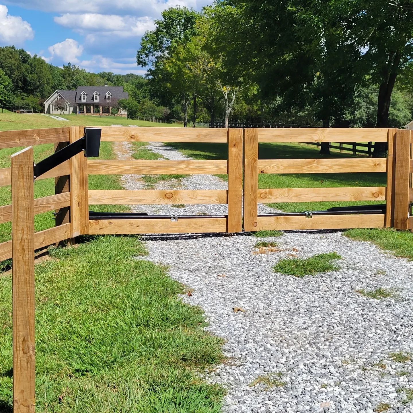 A wooden fence surrounds a gravel road leading to a house.