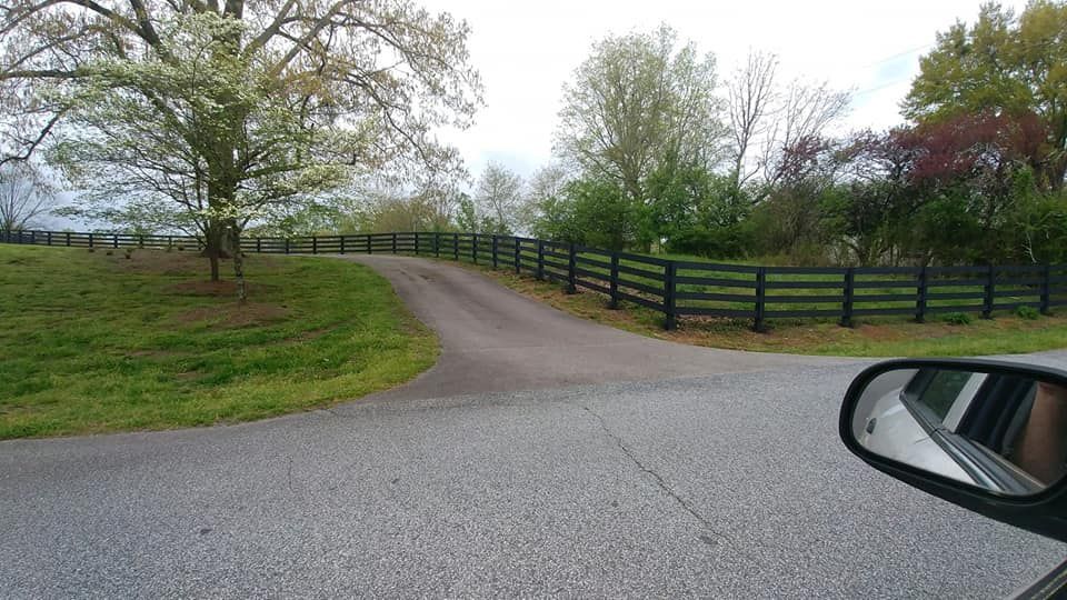 A car is driving down a road with a fence on the side