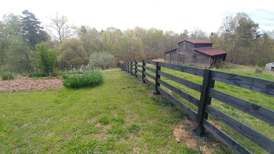 A black wooden fence surrounds a grassy field with a barn in the background.