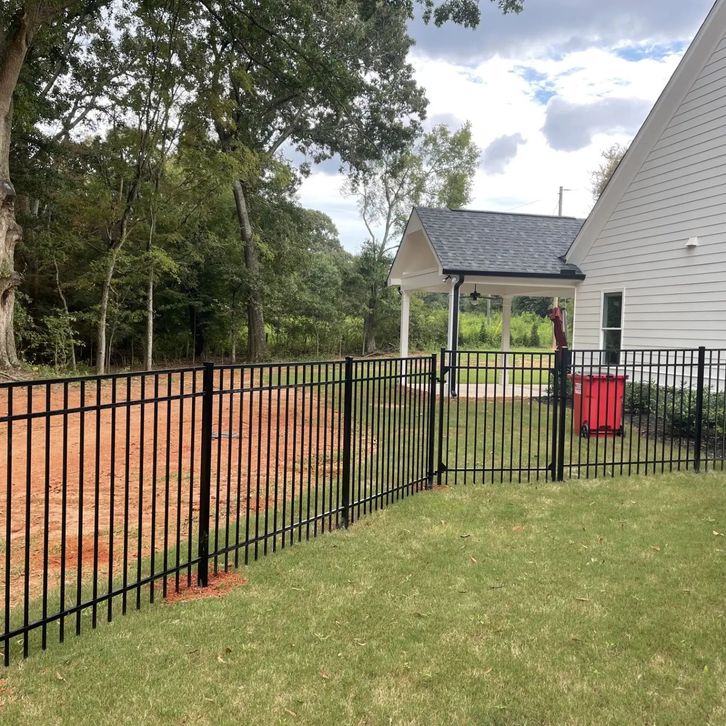 A black metal fence surrounds a lush green yard in front of a house.