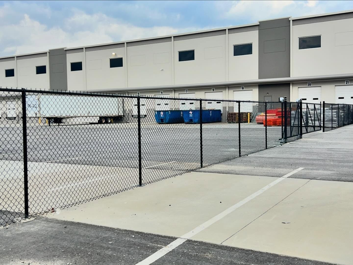 A chain link fence surrounds a parking lot in front of a large building