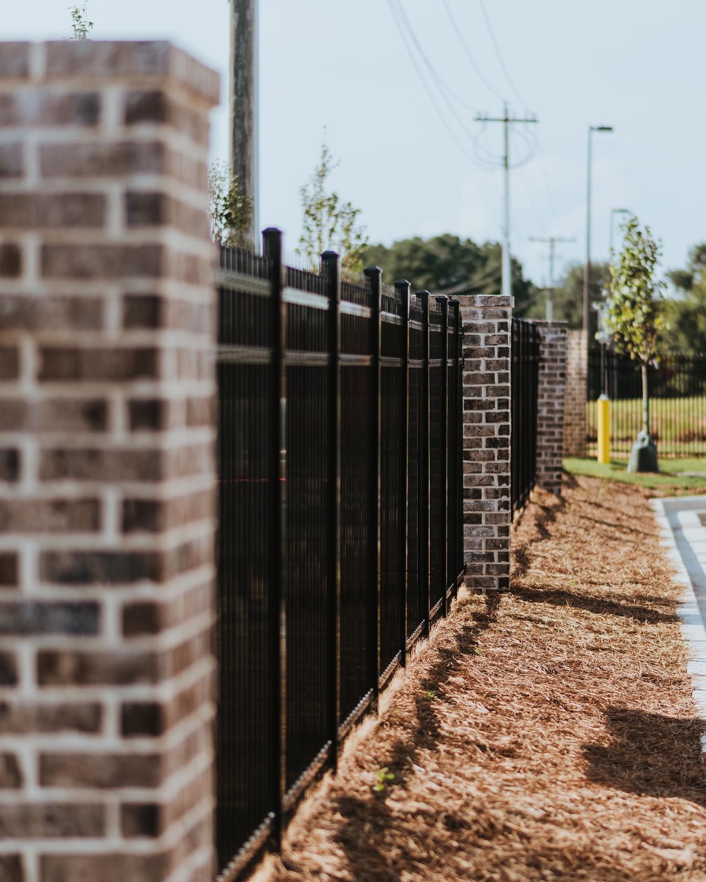 A black metal fence is surrounded by brick pillars.