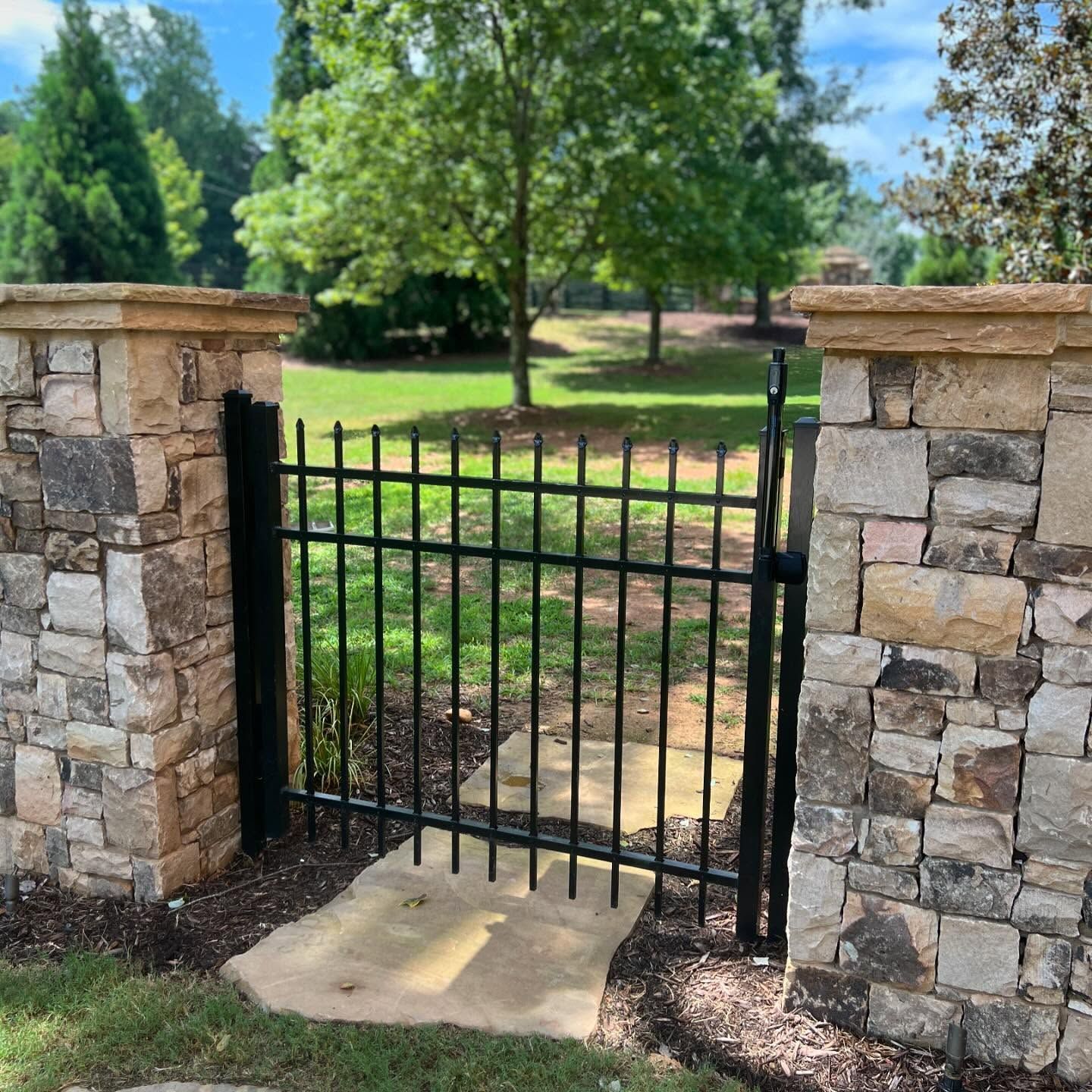 A stone wall with a metal gate leading to a park.