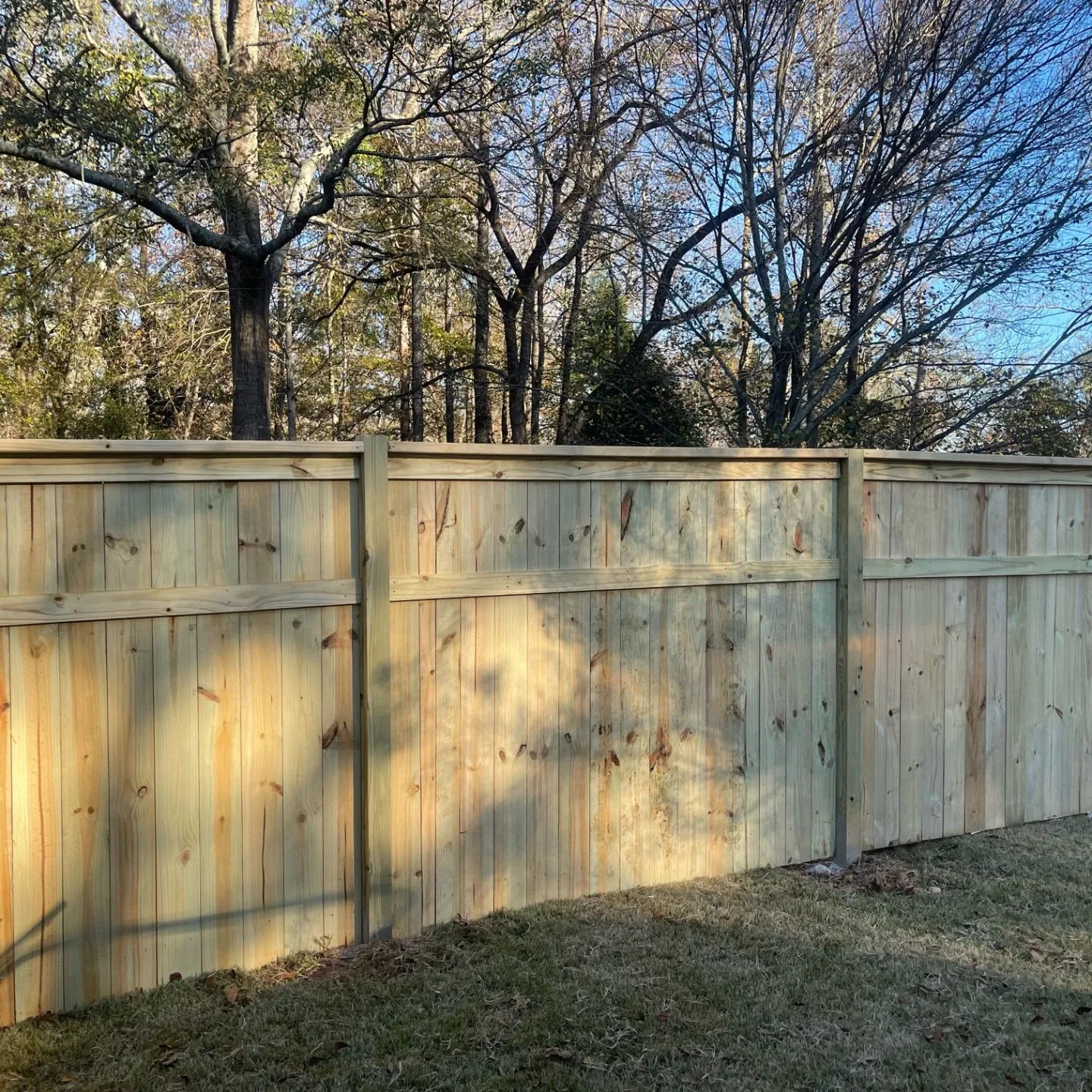 A wooden fence in a backyard with trees in the background.