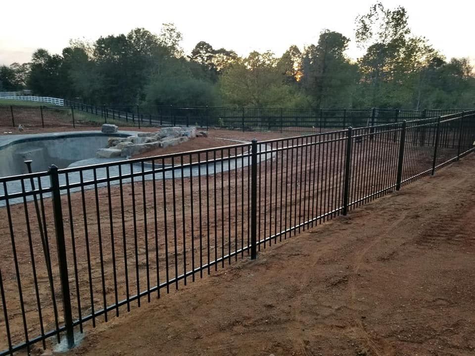 A black metal fence surrounds a swimming pool in a dirt field.