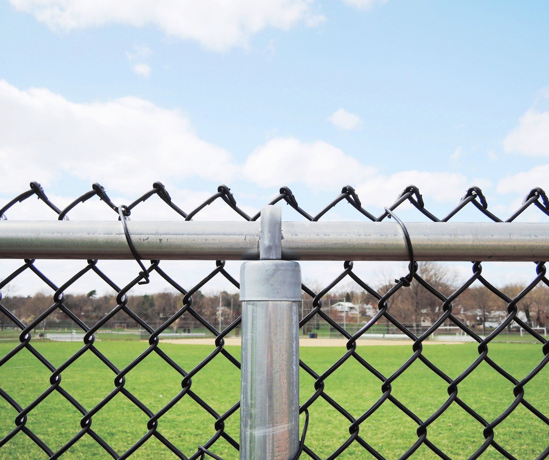 A chain link fence with a baseball field in the background