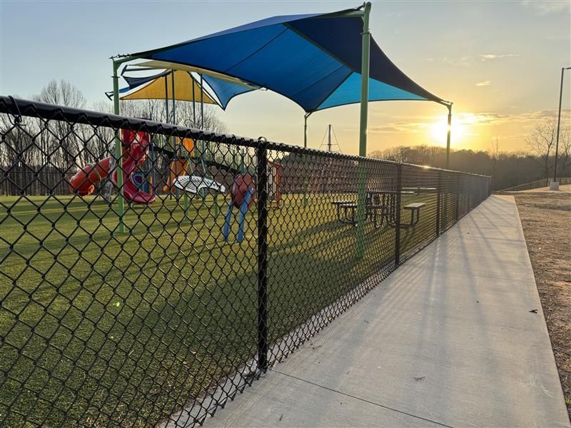 A chain link fence surrounds a playground at sunset