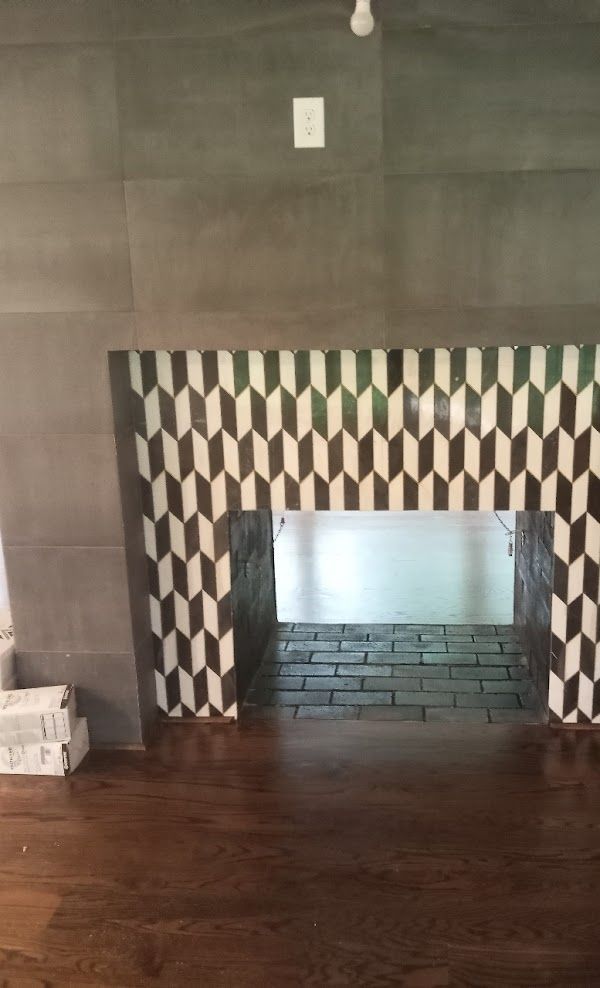 A fireplace with a patterned tile surround and a wooden floor in a living room.