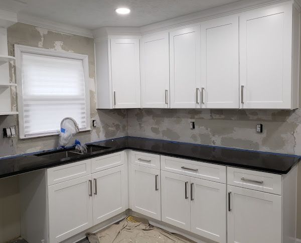 A kitchen with white cabinets and black counter tops is being remodeled