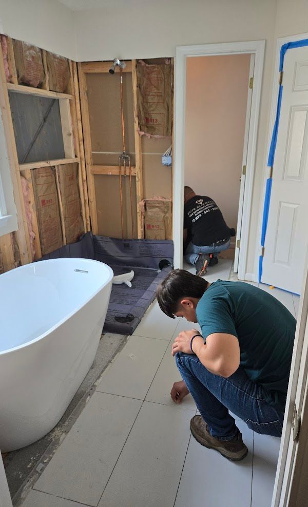 A man is kneeling in a bathroom next to a bathtub