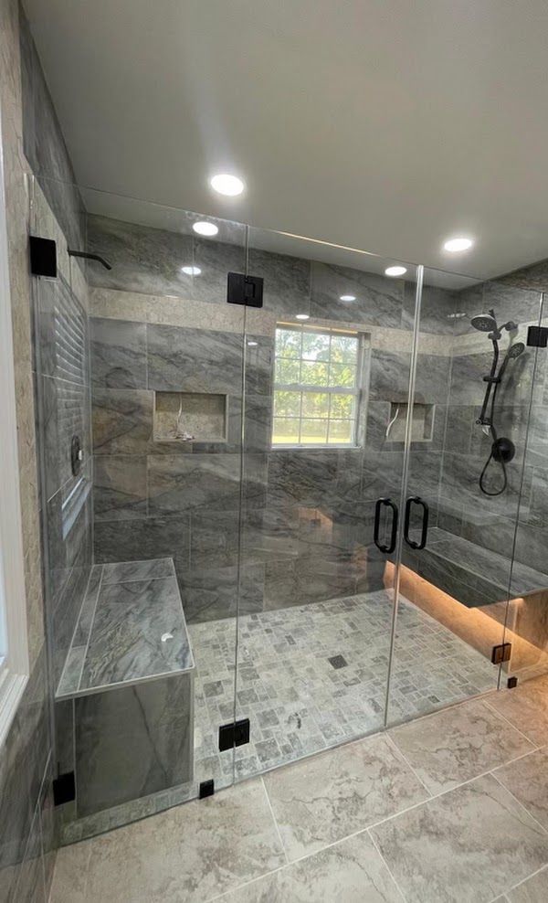A bathroom with a walk in shower with a bench and a window