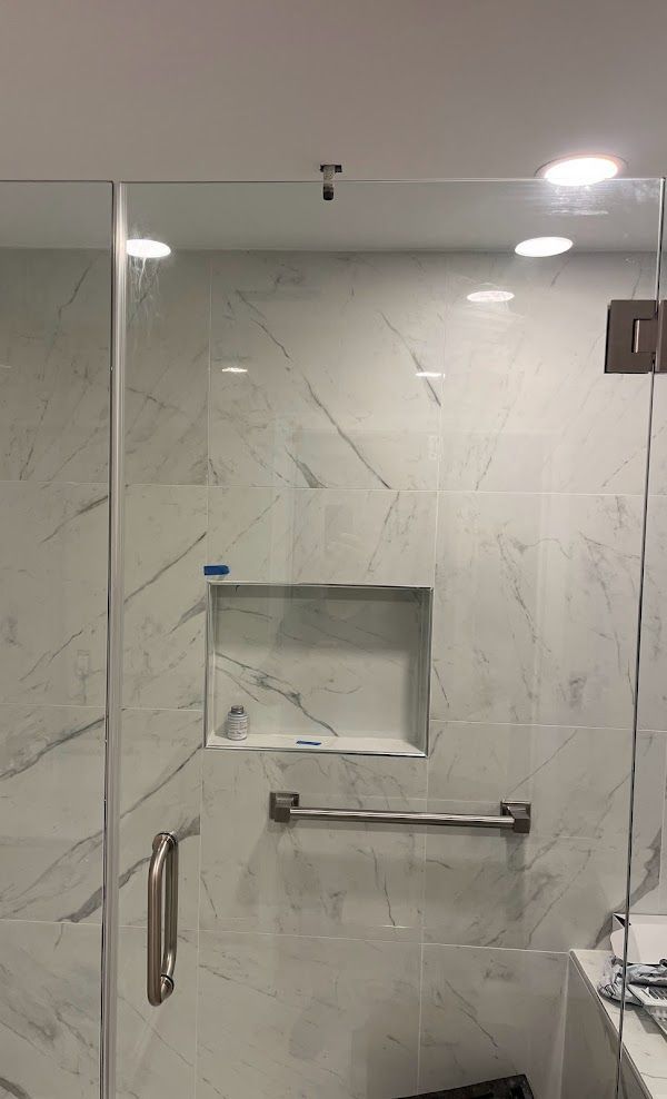 A bathroom with a glass shower door and a marble wall