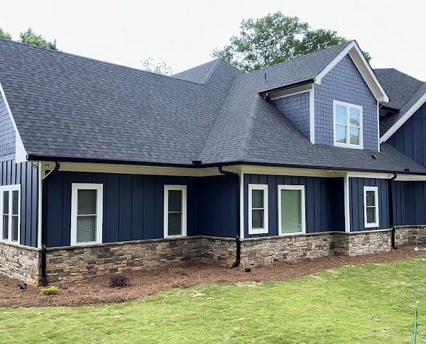 A blue house with a black roof and white windows is sitting on top of a lush green lawn