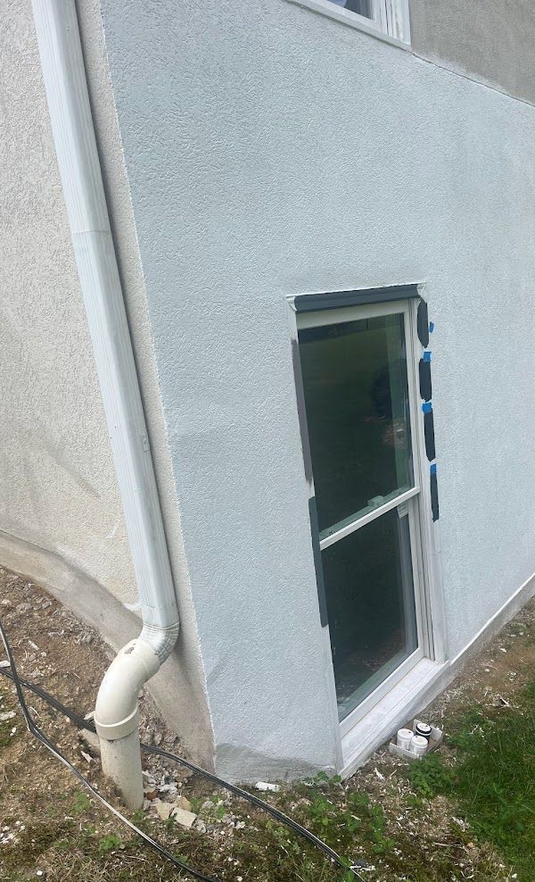 A white house with a window and a drain pipe on the side