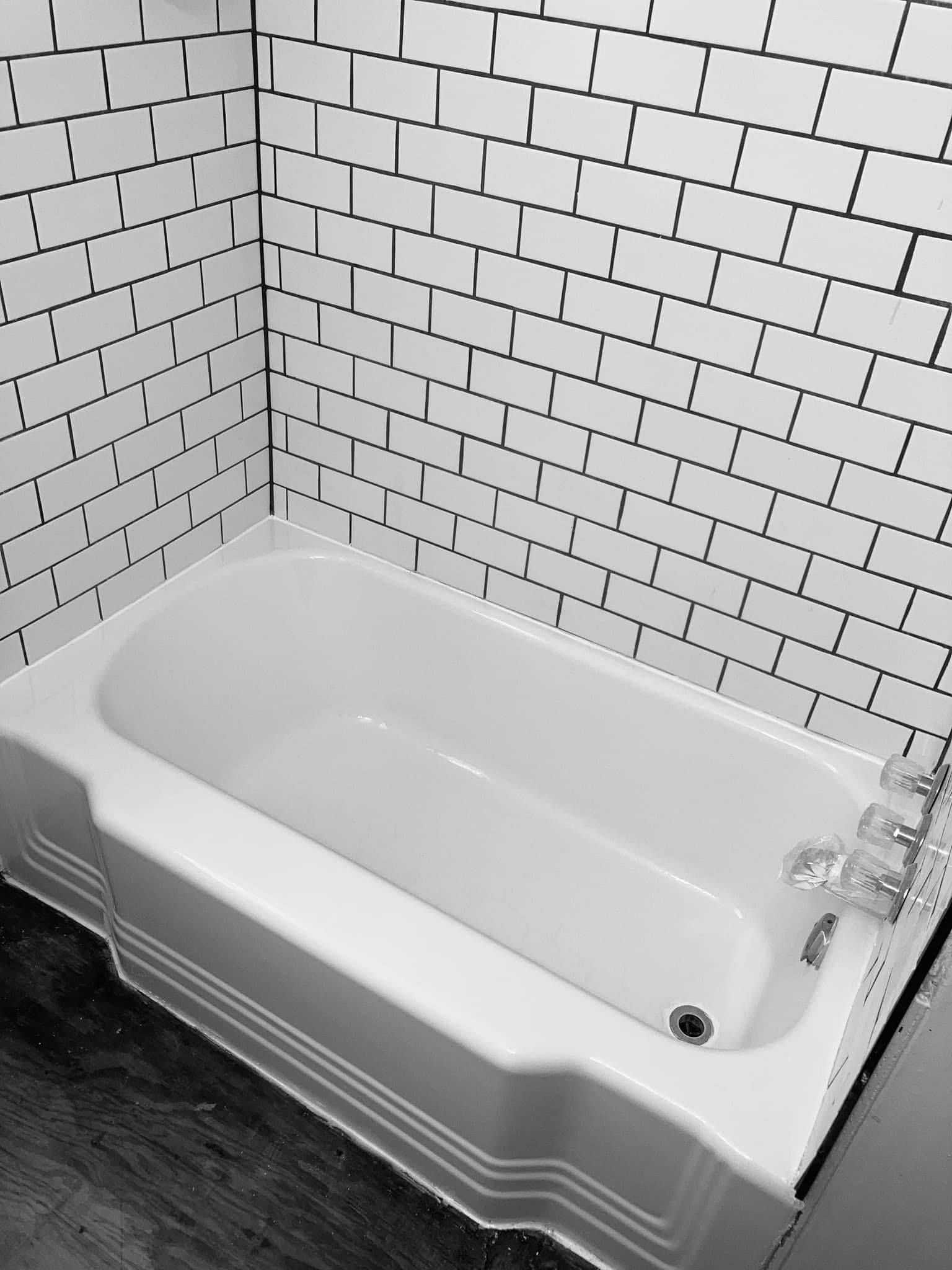 A white bathtub with white subway tile walls. Black grout lines define the tiles.
