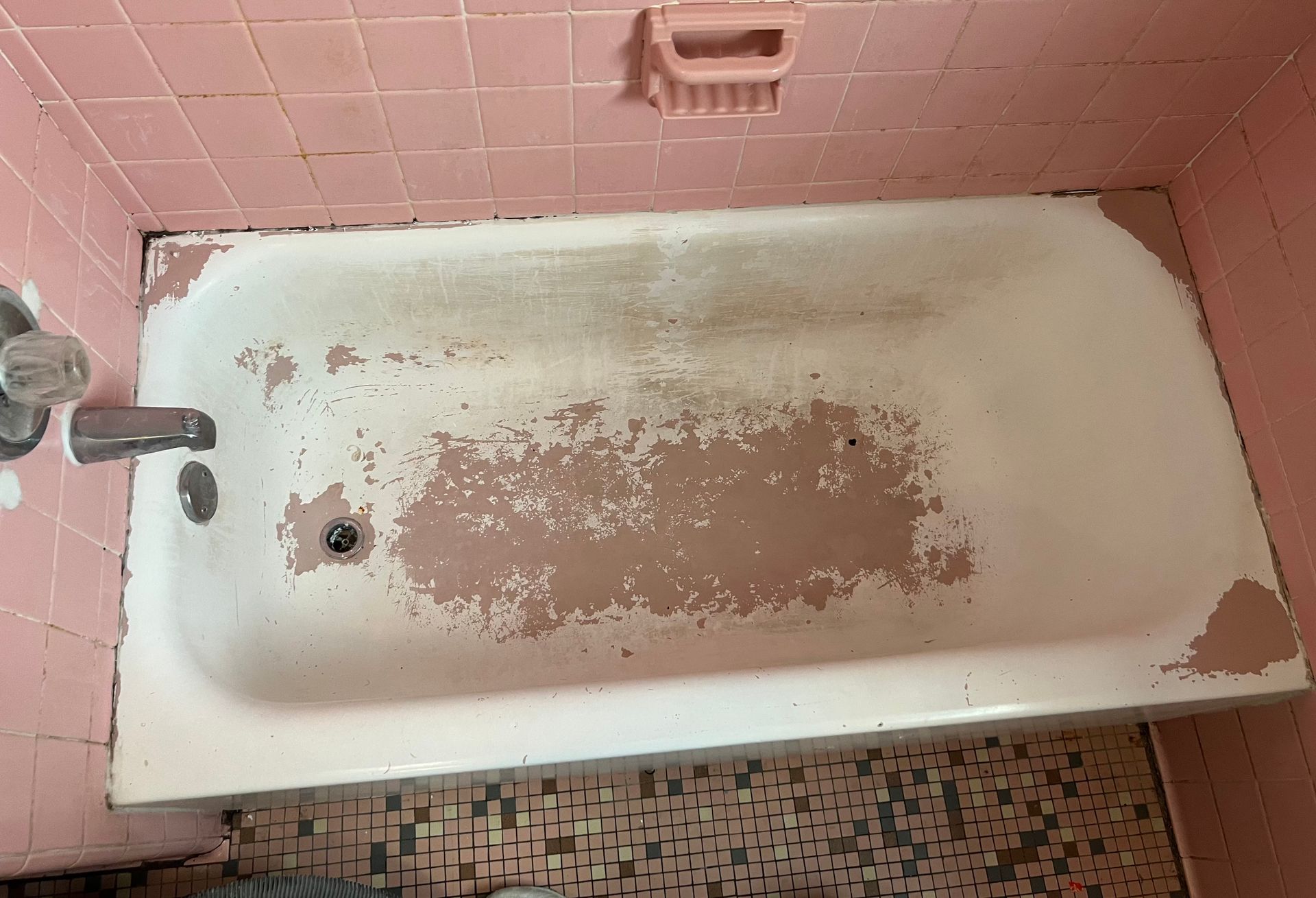 Pink-tiled bathroom with a worn, white bathtub. Patches of pink primer are visible through the chipped finish.