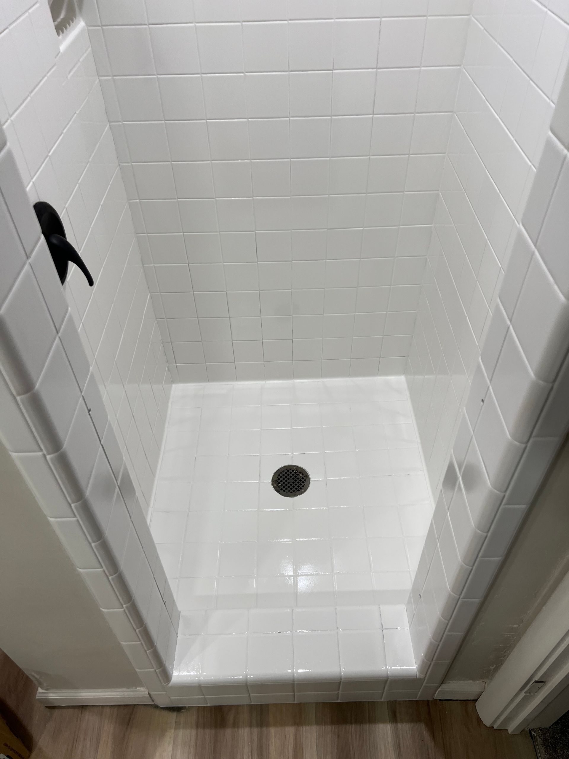 White tiled shower with black faucet, floor drain, and low threshold.