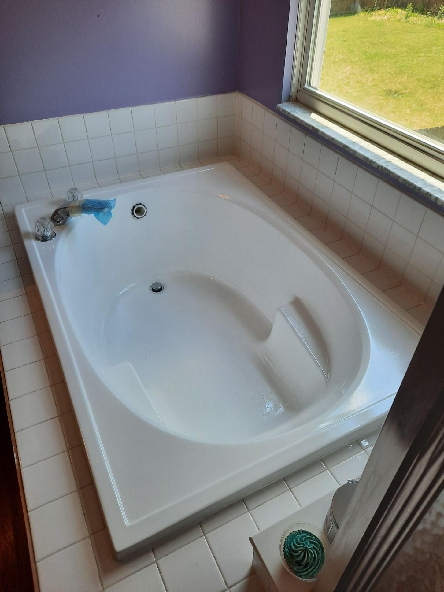 White built-in bathtub in a bathroom with tiled walls and a window.
