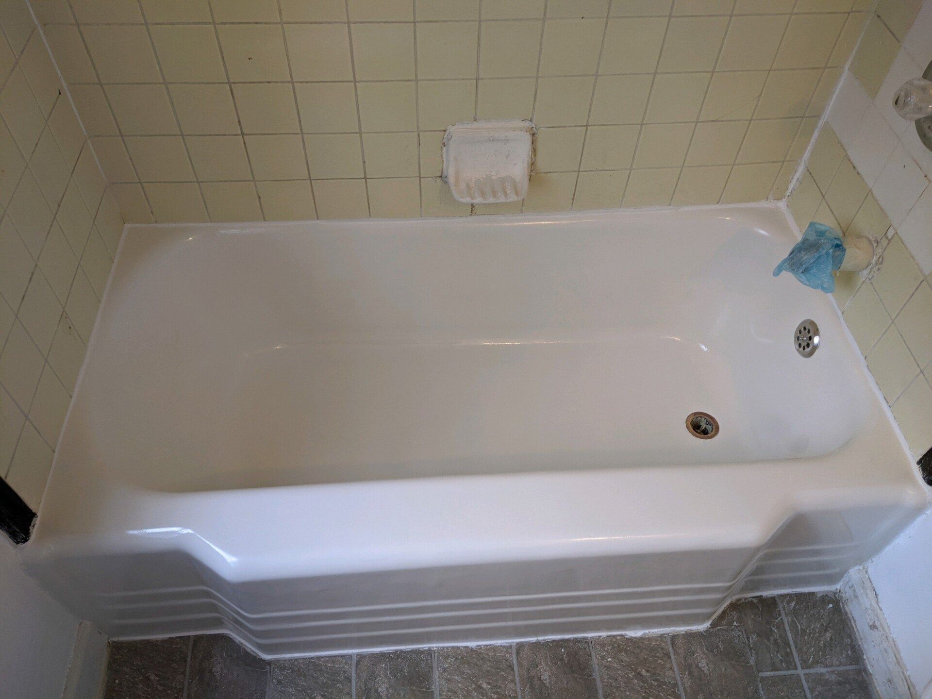 White bathtub with a soap dish, set in a tiled bathroom, with a damp cloth.