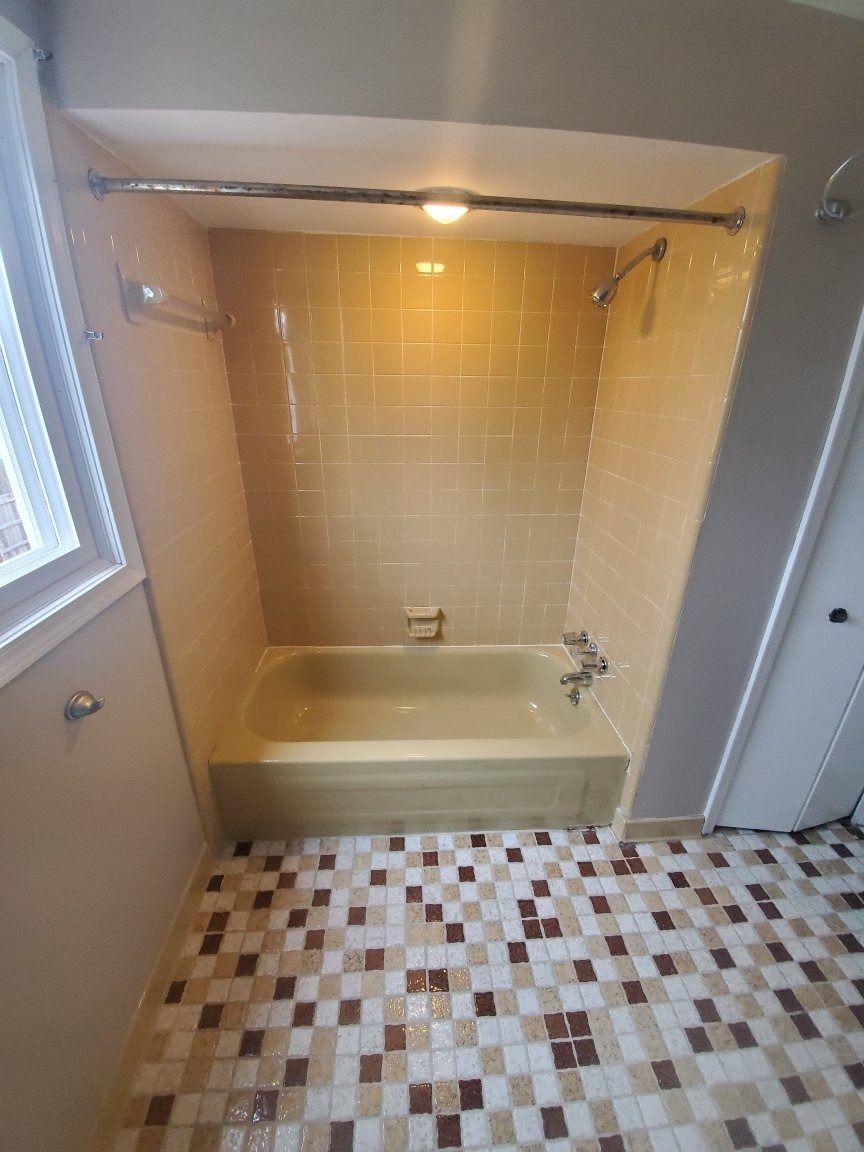 Bathroom with yellow tile shower/tub, brown/white mosaic floor, and a window.