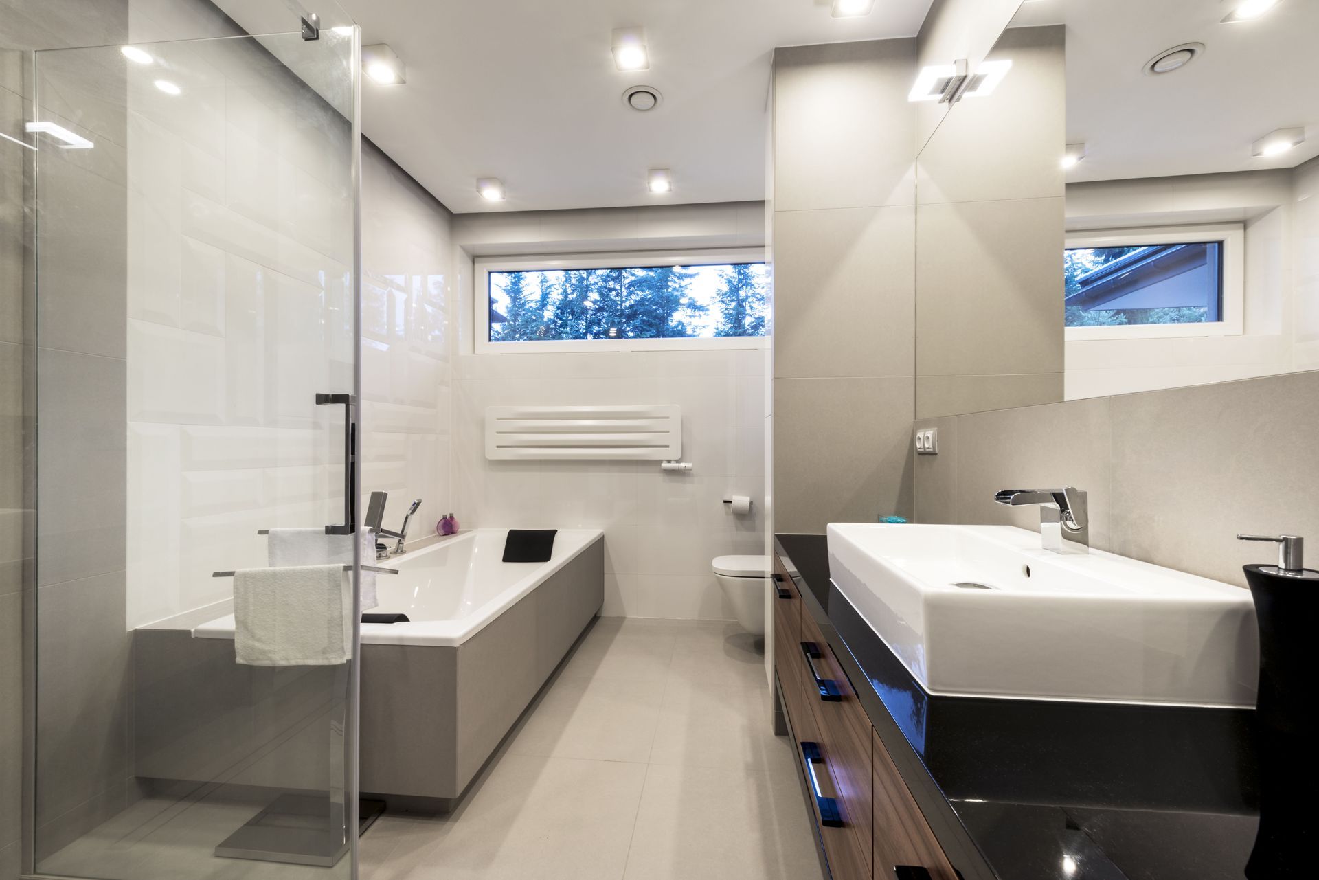 Modern bathroom with a bathtub, sink, toilet, and shower, featuring gray and white tones.