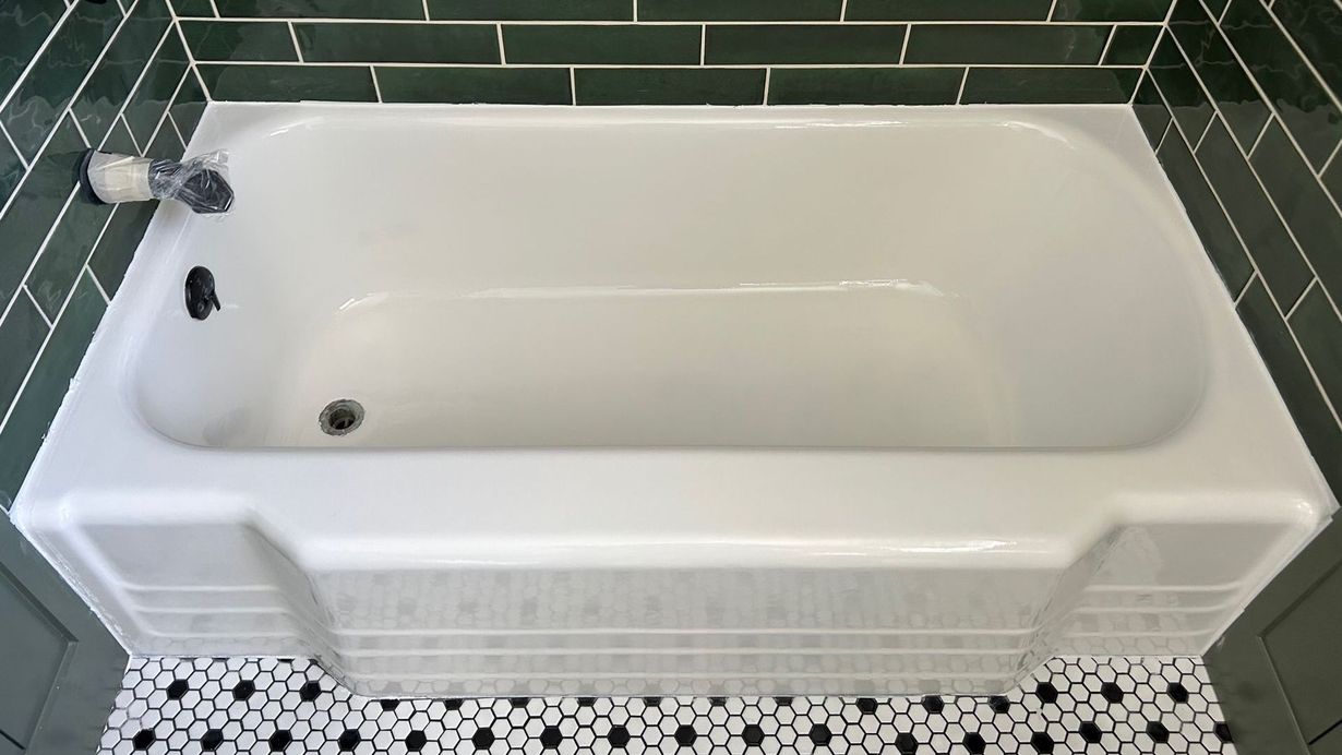 White bathtub set in a bathroom with dark green tiled walls and mosaic tiled floor.