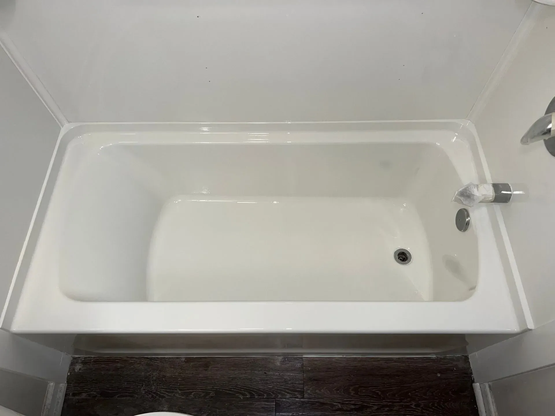 A white freestanding bathtub in a beige-tiled bathroom. A window and towels are also present.