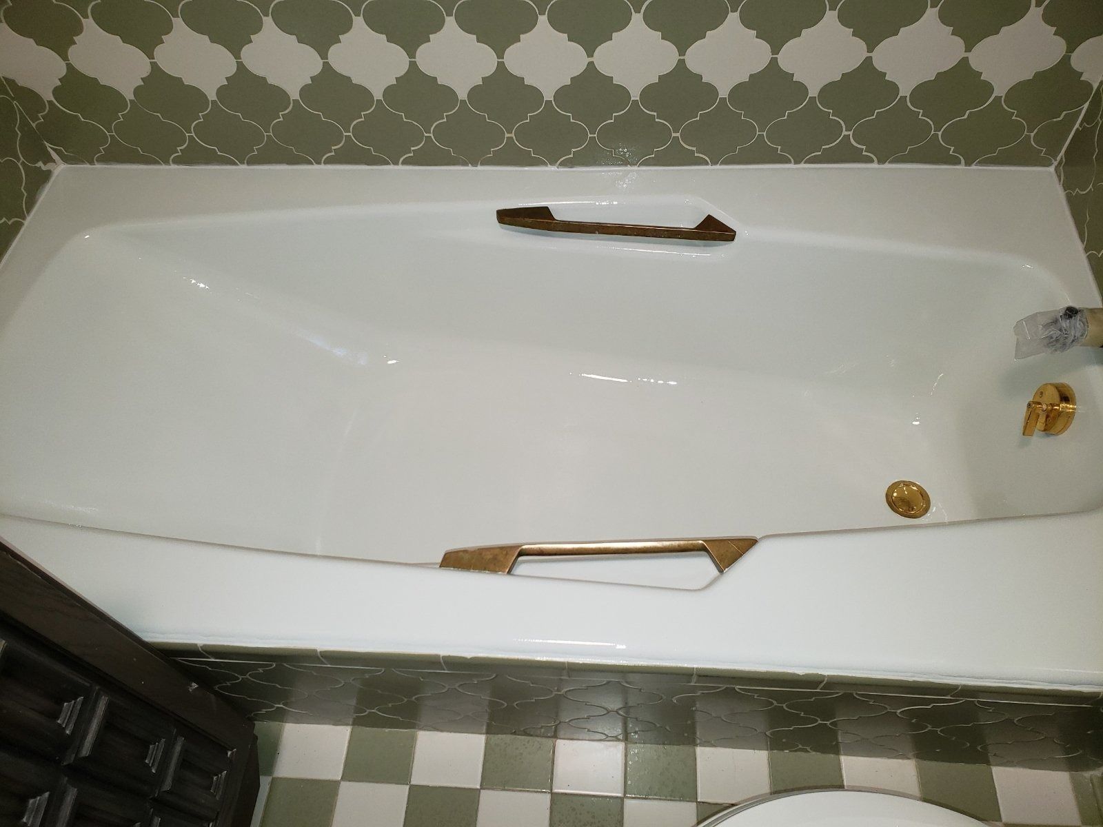White bathtub with gold fixtures, brown handles, and green tiled wall and floor.