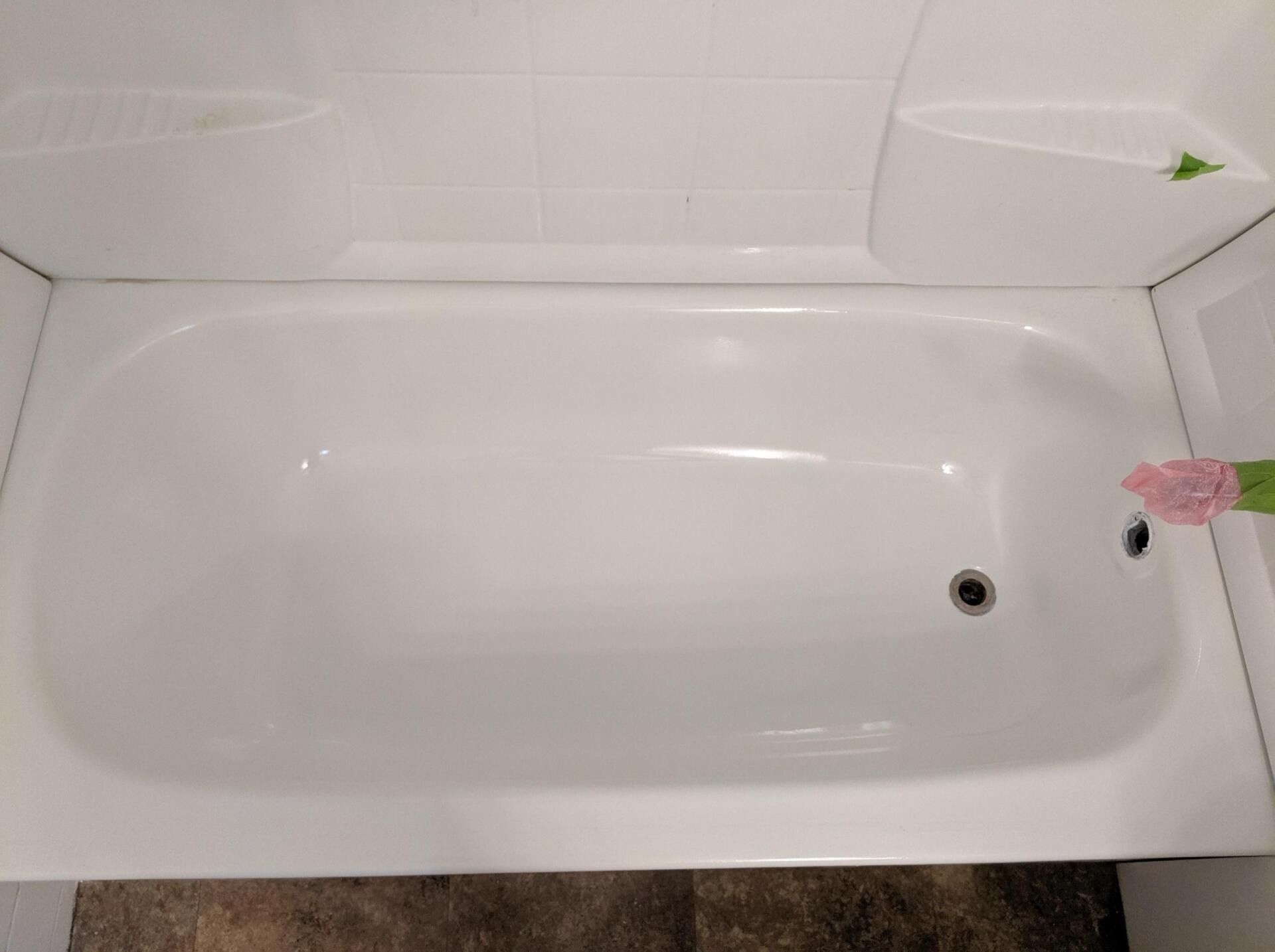White bathtub, surrounded by white tile and a small shelf, with a dark floor below.