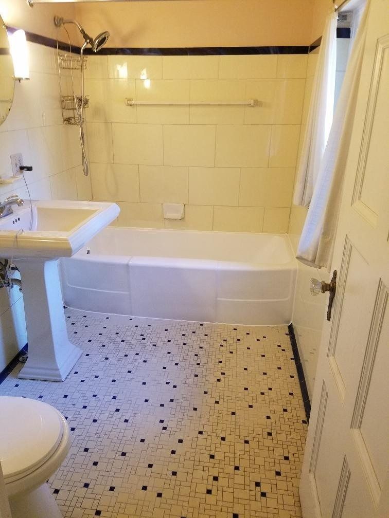 Bathroom with white fixtures, black and white tiled floor, and yellow-tiled walls, including a bathtub.