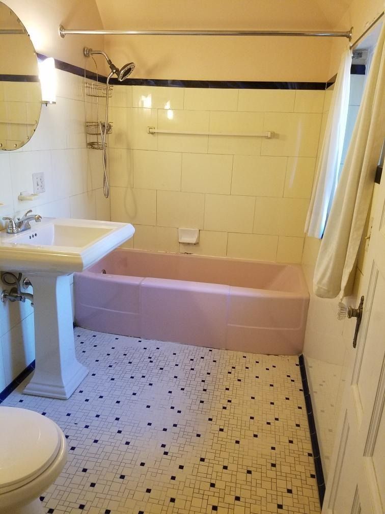 A retro bathroom with a pink tub and floor, white fixtures, and yellow walls.