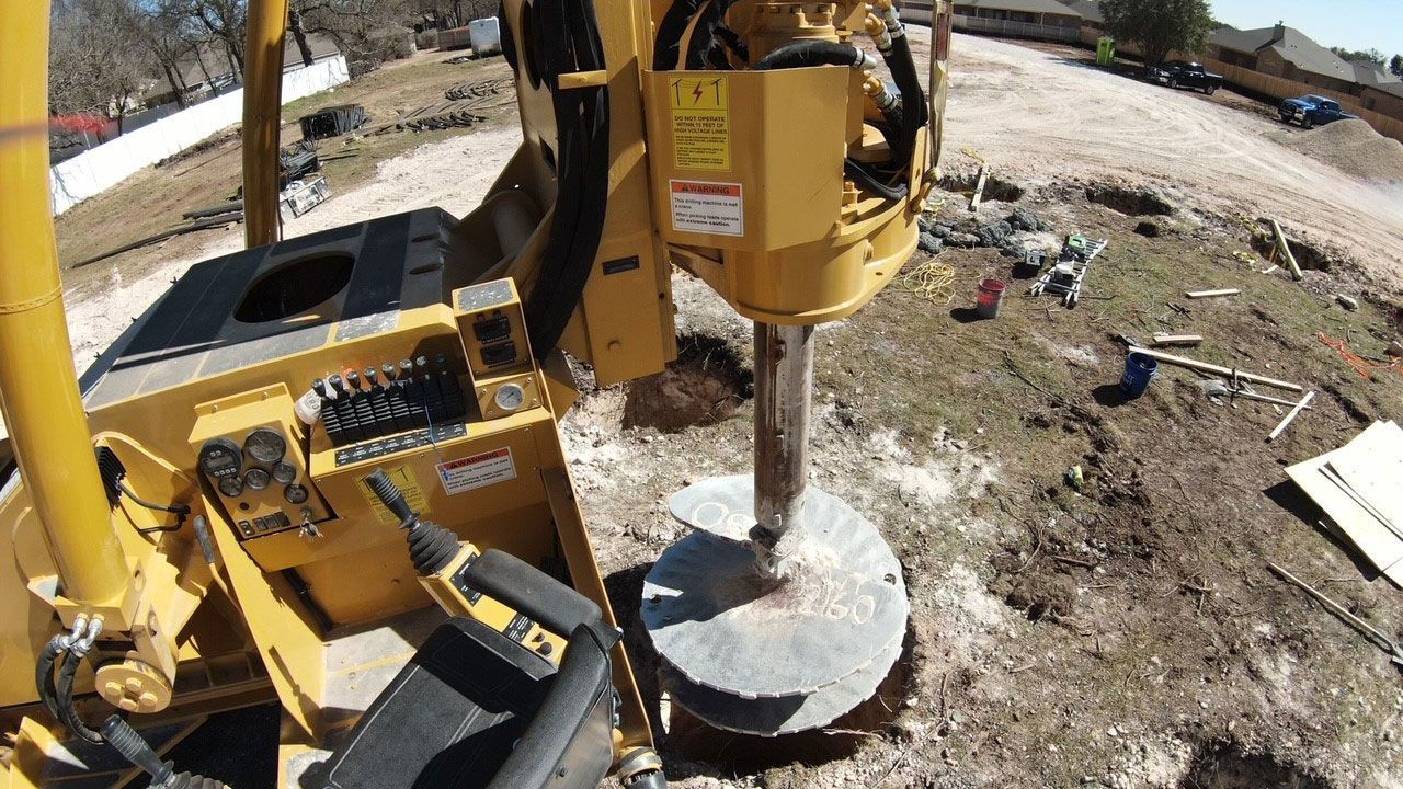 A yellow construction drill boring a hole into the dirt at a sunny, outdoor construction site.