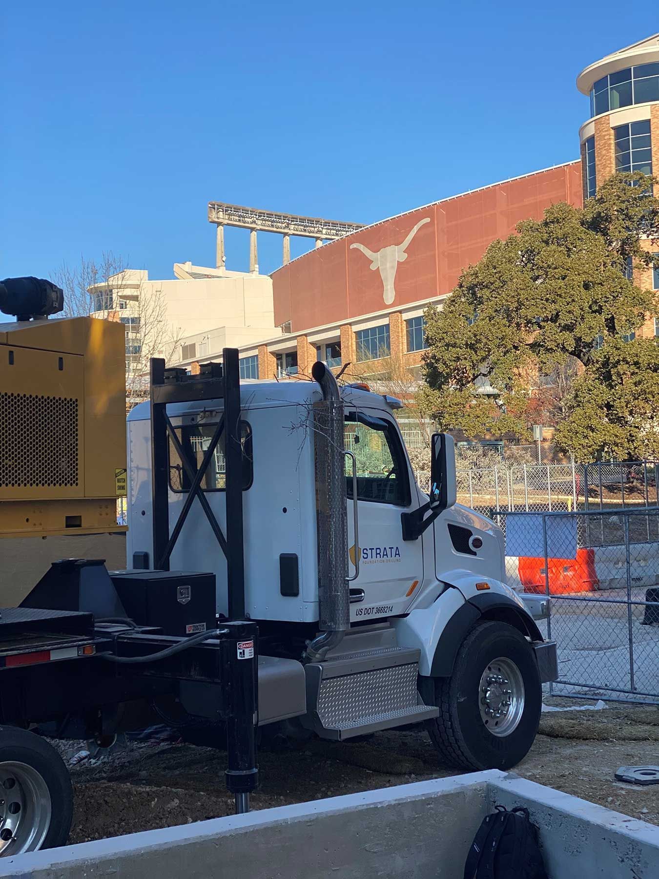 A white semi-truck parked in front of a building featuring a prominent Texas Longhorns logo under a clear blue sky.