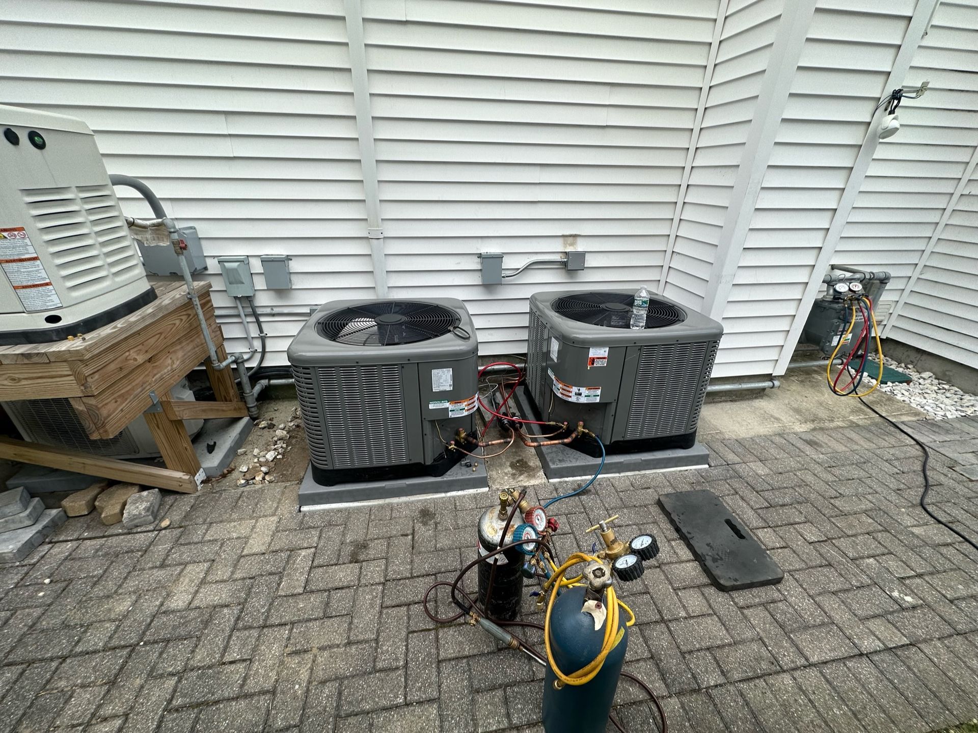 two air conditioners are sitting on a brick patio in front of a house .