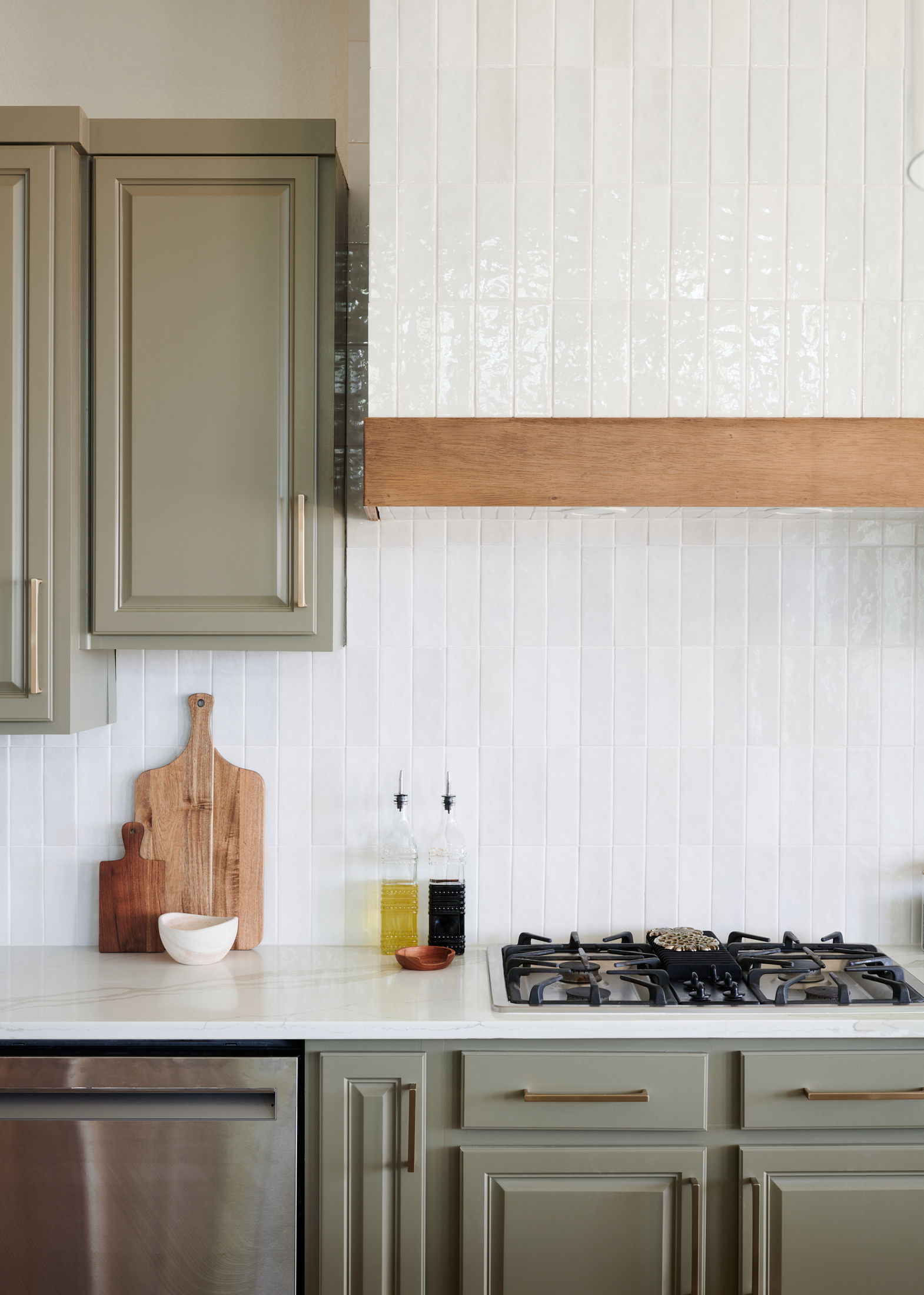 A kitchen with green cabinets , a stove , a dishwasher , and a wooden hood.