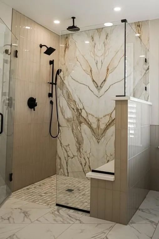 A modern shower with marble and neutral-toned tiles. Black fixtures contrast the light-colored walls and flooring.