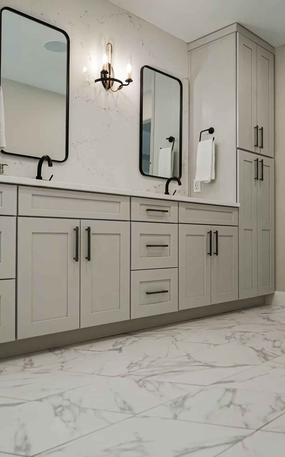 Modern bathroom with light gray cabinets, marble-patterned floors, two black-framed mirrors, and a decorative wall sconce.