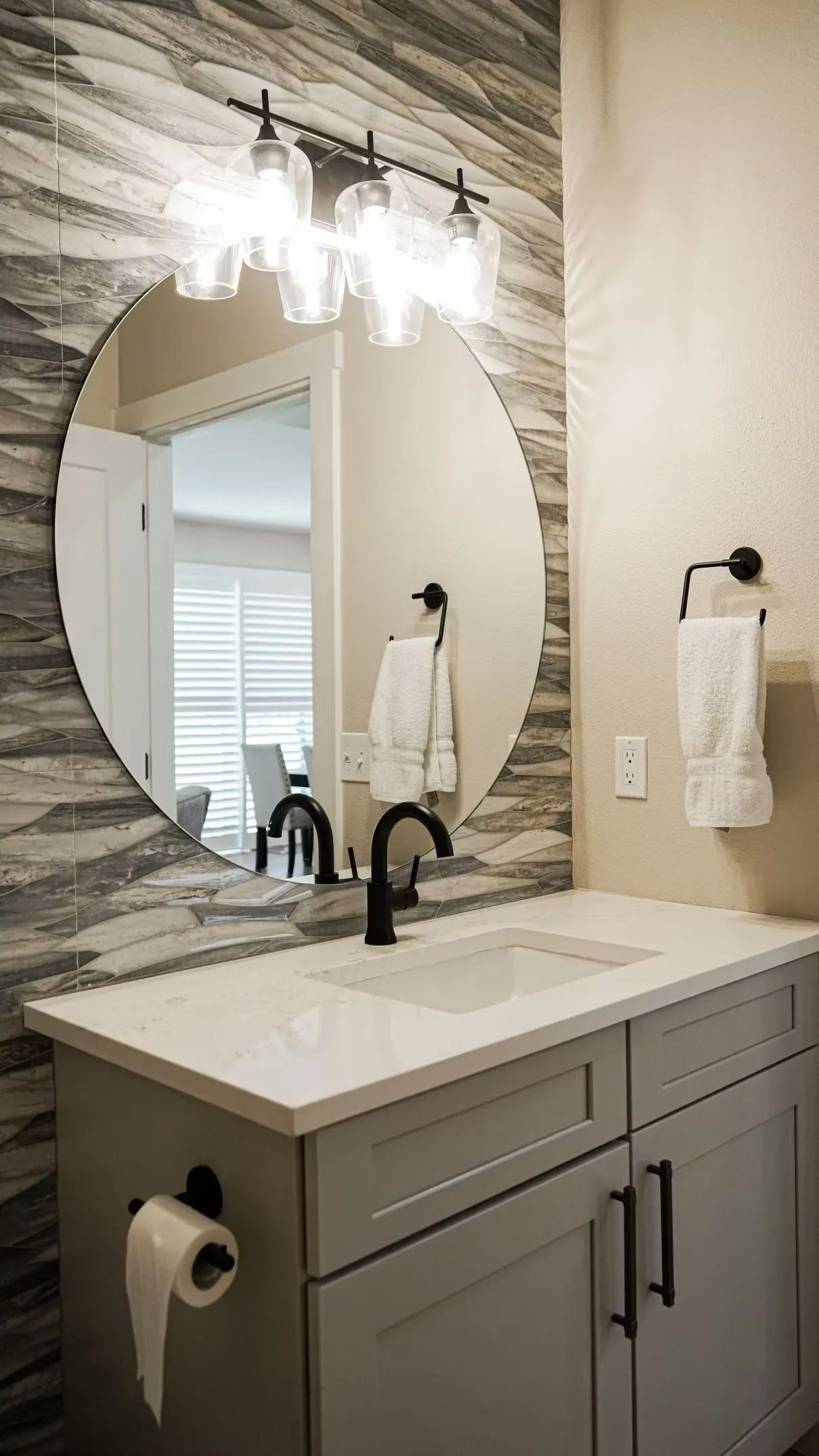 Bathroom with a round mirror, vanity, and decorative wall. Gray and white color scheme.
