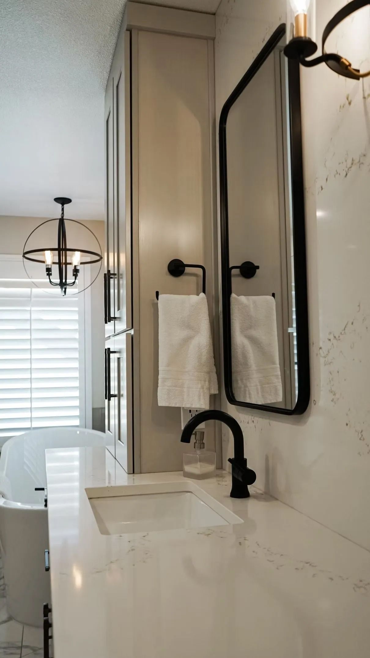 Bathroom with a black-framed mirror, white quartz countertop, and a black faucet. White towels hang on a black bar.