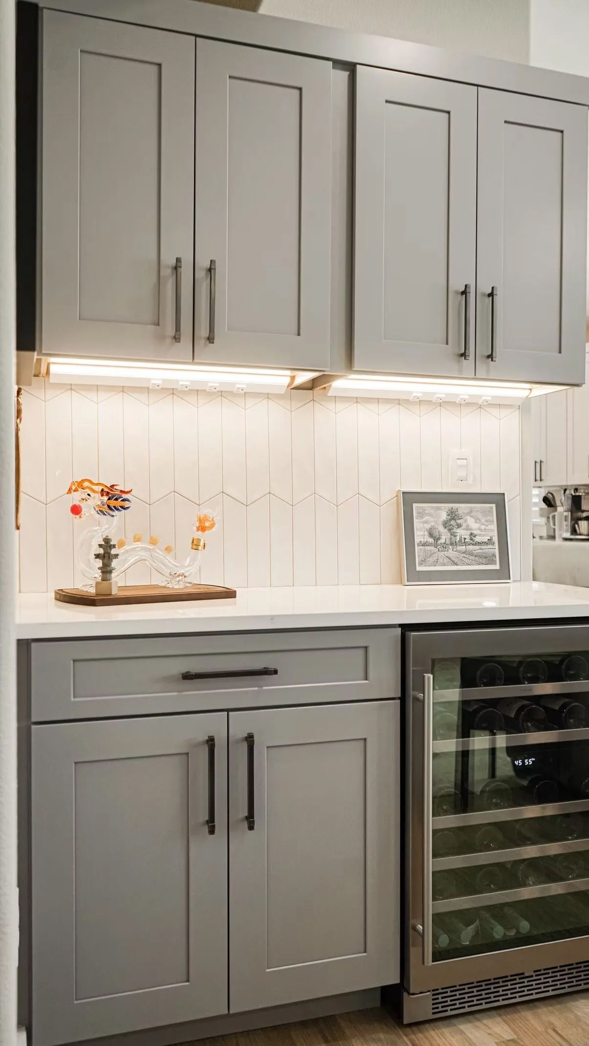 Gray kitchen cabinets with a wine fridge, white countertops, and under-cabinet lighting.