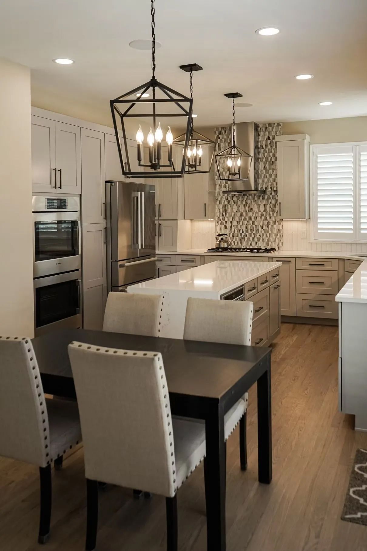 Modern kitchen with a large island, light gray cabinets, stainless steel appliances, and a dark dining table with upholstered chairs.