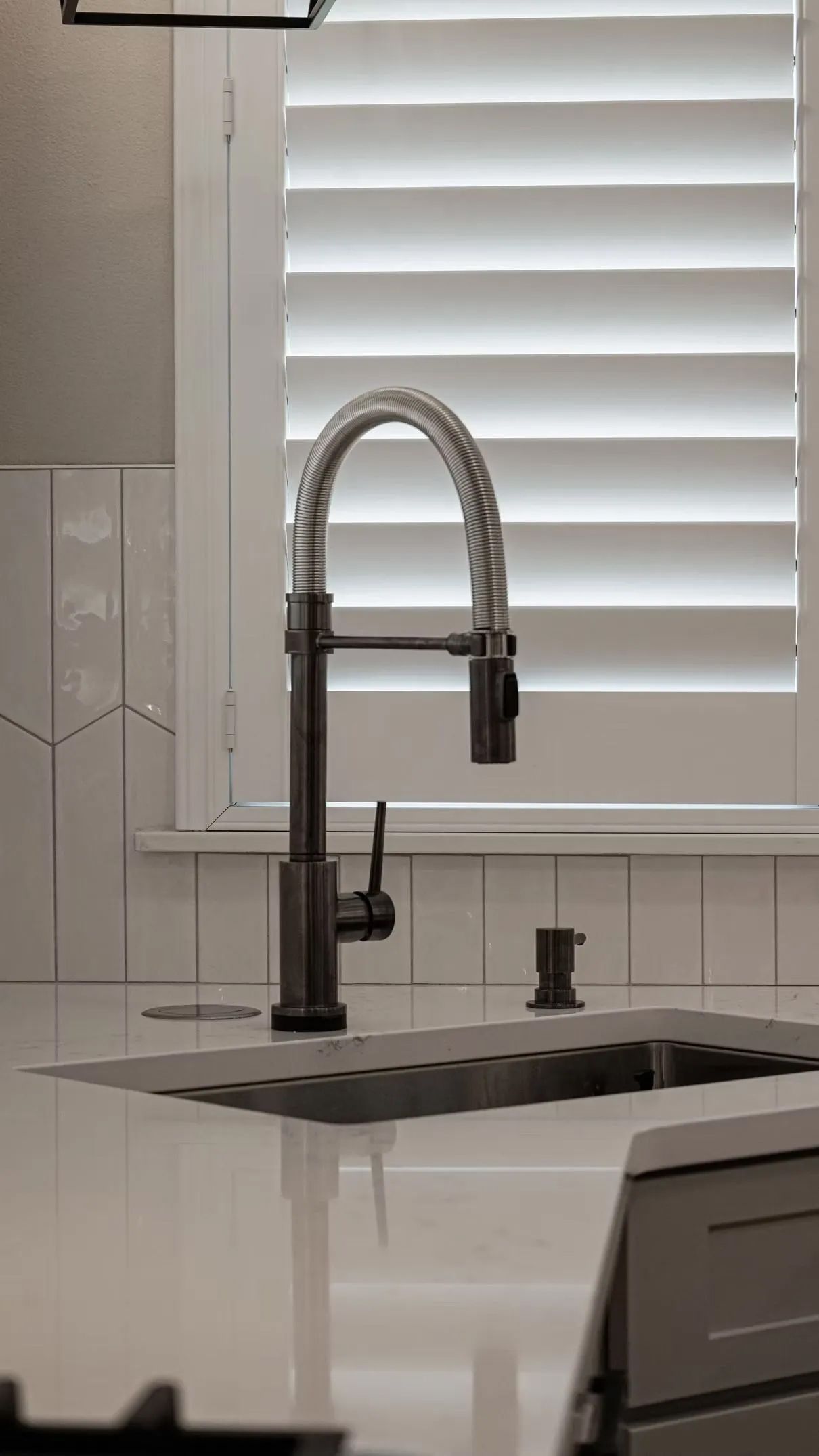 Kitchen faucet with a flexible coiled neck, in front of a window with white shutters.
