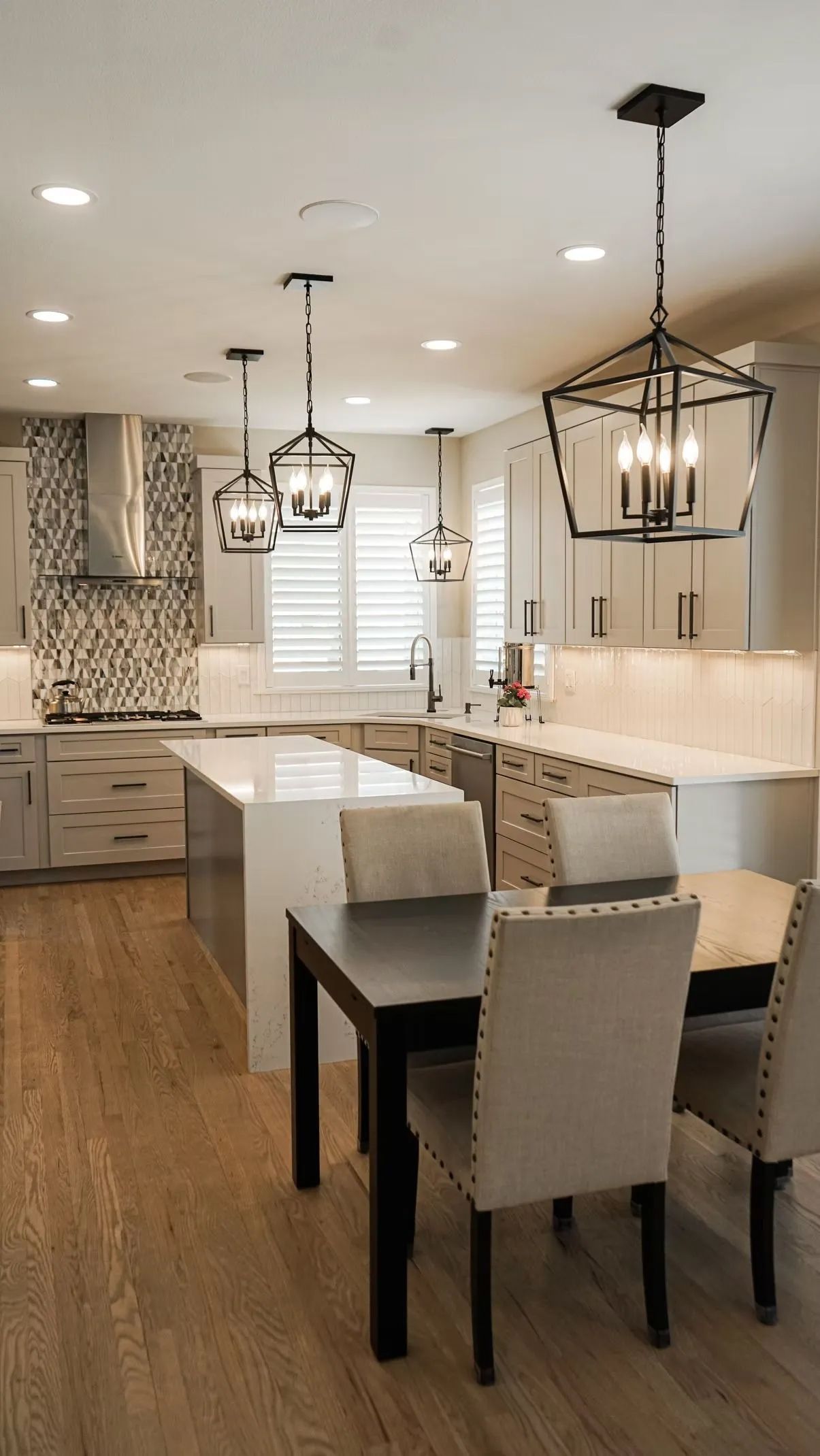 Modern kitchen with light wood floors, island, and dining table with upholstered chairs under pendant lights.