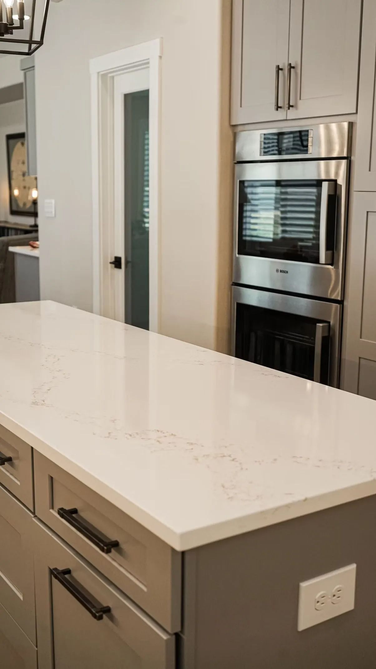 Kitchen island with white countertop and gray cabinets. Stainless steel oven and upper cabinets in the background.