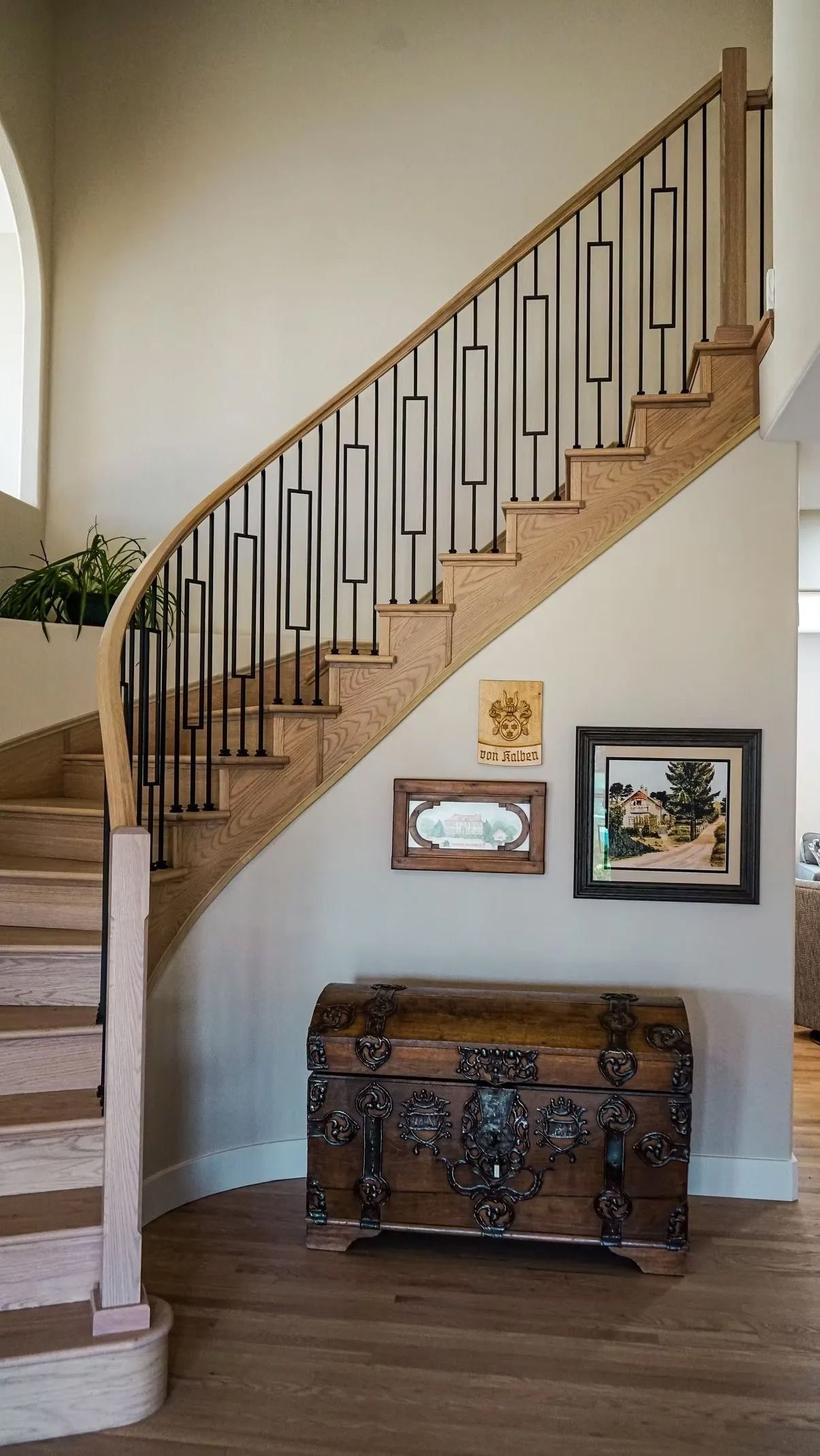 Wooden staircase with black vertical balusters, ascending to the right. A decorative chest sits below framed artwork.